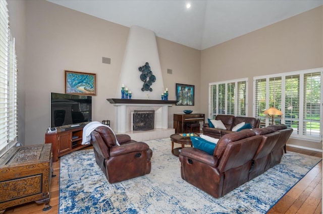living room with high vaulted ceiling, a tiled fireplace, and hardwood / wood-style flooring