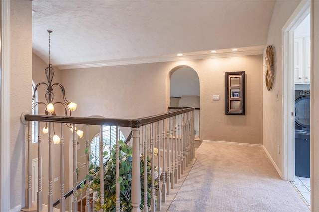 hallway with light colored carpet, arched walkways, a chandelier, baseboards, and ornamental molding