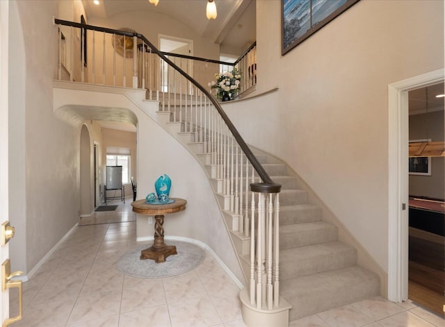 stairway featuring arched walkways, baseboards, and a towering ceiling