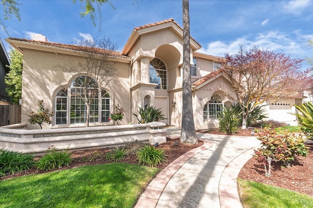 mediterranean / spanish home with fence, a tiled roof, and stucco siding