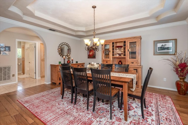 dining space with visible vents, a tray ceiling, arched walkways, light wood-style flooring, and a notable chandelier