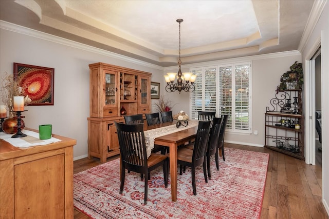 dining space with an inviting chandelier, a raised ceiling, ornamental molding, and wood-type flooring