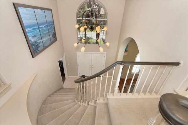 stairway with arched walkways, a high ceiling, baseboards, and a notable chandelier