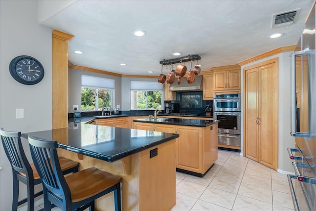 kitchen featuring visible vents, dark countertops, double oven, an island with sink, and a warming drawer