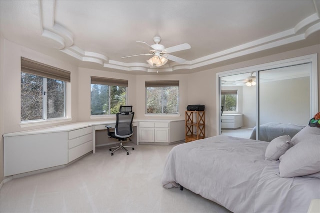 bedroom featuring built in desk, a tray ceiling, multiple windows, and light carpet