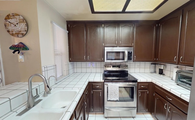 7186 N Gregory Ave, Fresno, CA 93722 - kitchen with stainless steel appliances, tile countertops, a sink, tasteful backsplash, and dark brown cabinets