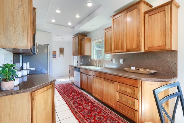 kitchen featuring light tile patterned flooring, a raised ceiling, stainless steel dishwasher, a sink, and backsplash