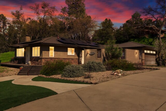 view of front facade featuring a chimney, a garage, concrete driveway, and roof mounted solar panels