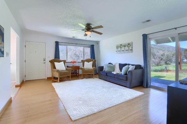 living room featuring baseboards, a textured ceiling, light wood-style floors, ceiling fan, and visible vents