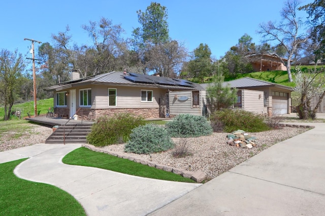 view of front of home with driveway, stone siding, a chimney, solar panels, and a garage