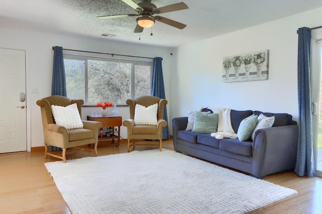 living room featuring visible vents, a textured ceiling, light wood-style floors, and ceiling fan
