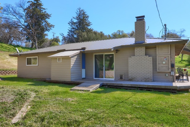 back of property with a wooden deck, a chimney, a lawn, and metal roof