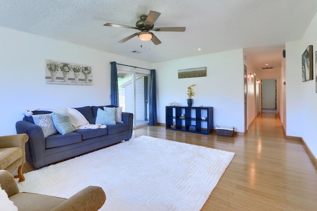 living room with visible vents, a textured ceiling, light wood finished floors, and ceiling fan