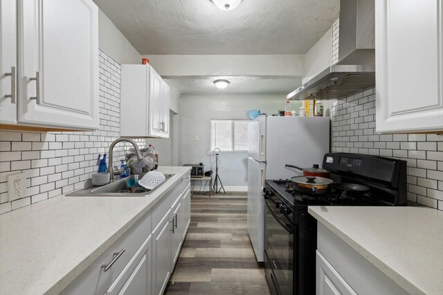 kitchen with white cabinets, a sink, dark wood-style floors, wall chimney range hood, and black gas range