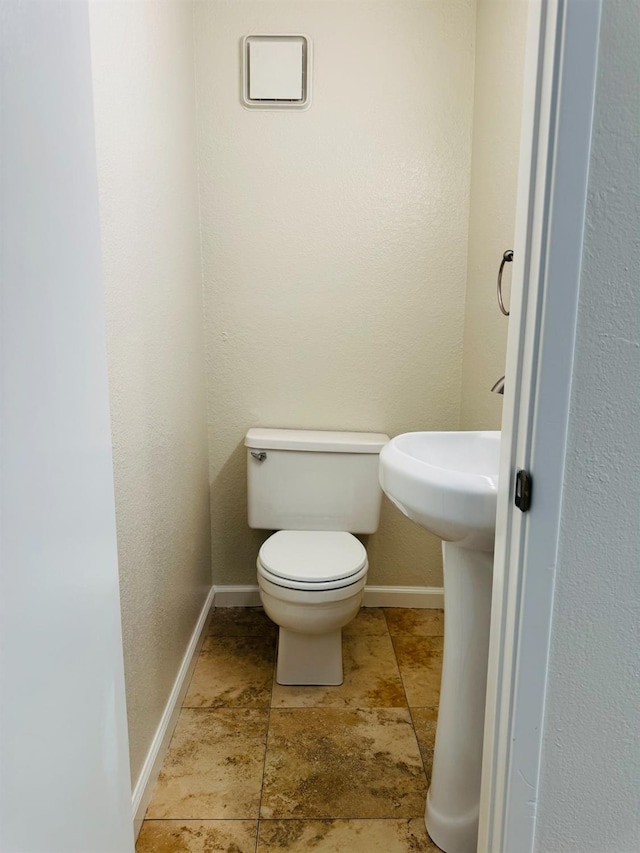 half bathroom with baseboards, stone finish flooring, and toilet