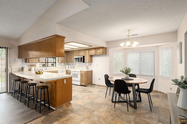 kitchen with an inviting chandelier, white appliances, a peninsula, a textured ceiling, and tile counters