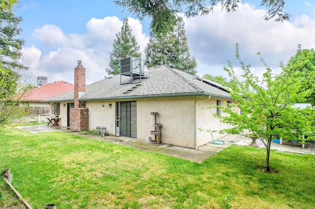 back of house featuring a shingled roof, a patio area, a lawn, fence, and stucco siding