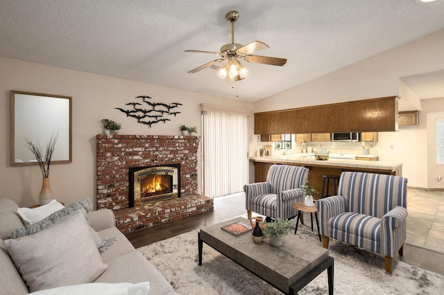 living room featuring ceiling fan, a textured ceiling, vaulted ceiling, and a fireplace