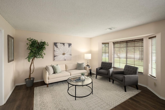 living room with a textured ceiling, wood finished floors, baseboards, and visible vents