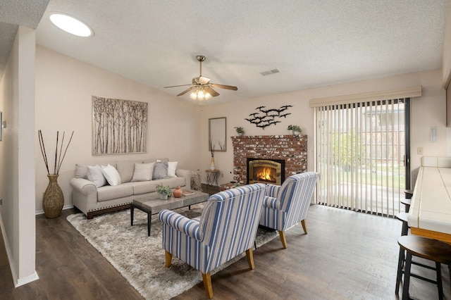 living area with dark wood-style floors, a textured ceiling, a ceiling fan, visible vents, and a brick fireplace