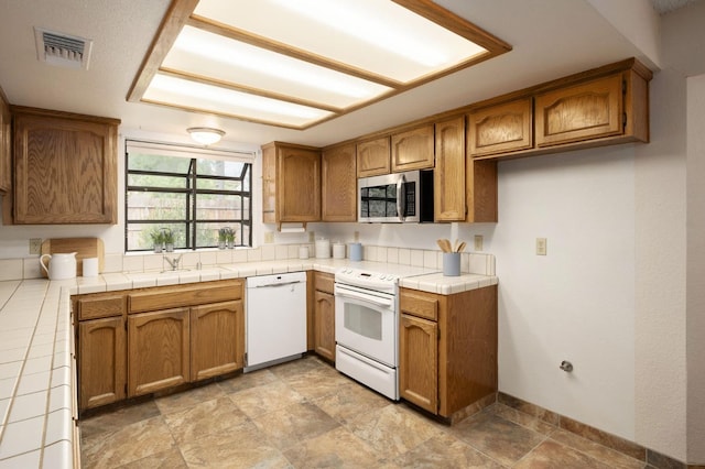 kitchen with visible vents, a sink, white appliances, brown cabinets, and tile countertops