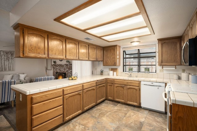 kitchen with a peninsula, visible vents, stainless steel microwave, a sink, and white dishwasher