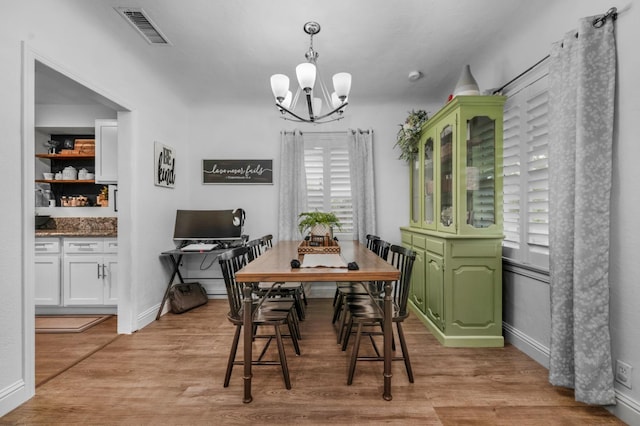 dining area featuring baseboards, visible vents, light wood-type flooring, and an inviting chandelier