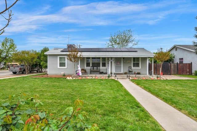 ranch-style home featuring covered porch, a front yard, fence, and roof mounted solar panels
