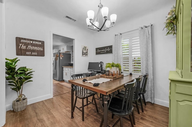 dining room featuring baseboards, visible vents, wood finished floors, and an inviting chandelier