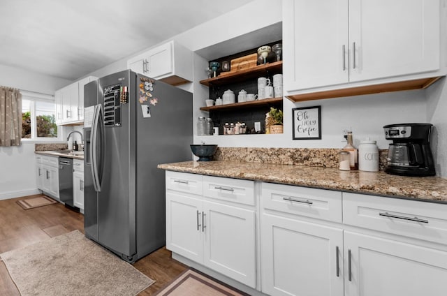 kitchen featuring light stone countertops, wood finished floors, stainless steel appliances, white cabinetry, and a sink