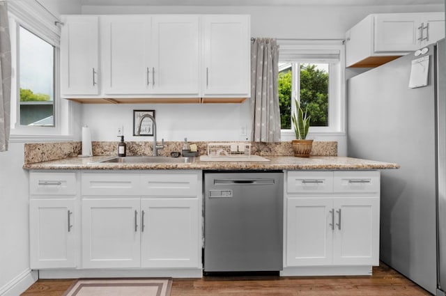 kitchen featuring white cabinets, a sink, stainless steel appliances, and light stone counters