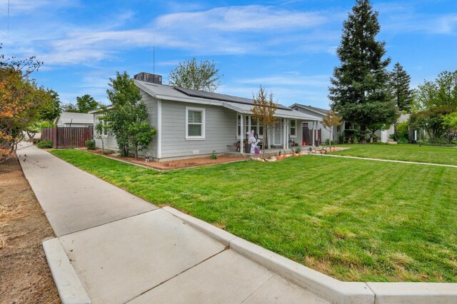 ranch-style house featuring roof mounted solar panels, a front yard, covered porch, and fence