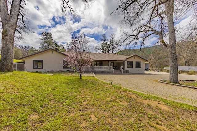 back of house with stucco siding, covered porch, and a yard