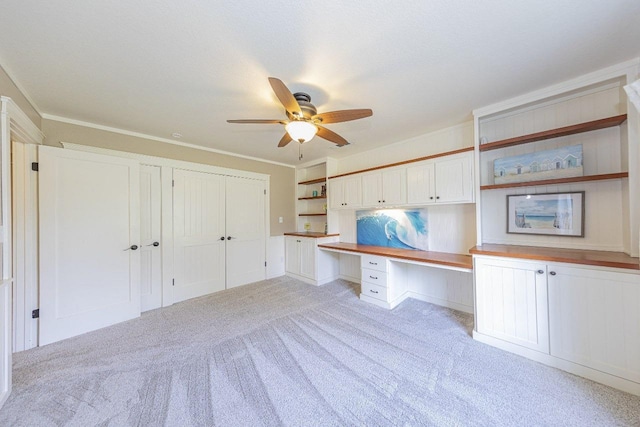 unfurnished office featuring light carpet, crown molding, ceiling fan, and built in study area