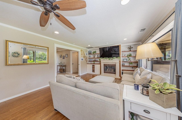 living area featuring visible vents, crown molding, baseboards, light wood-type flooring, and a glass covered fireplace