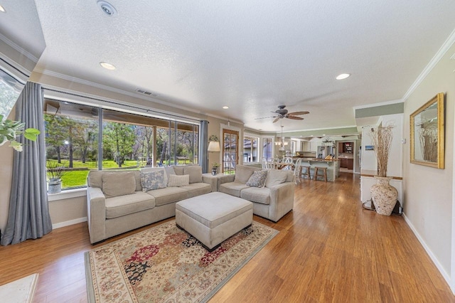 living room with crown molding, a ceiling fan, wood finished floors, a textured ceiling, and visible vents