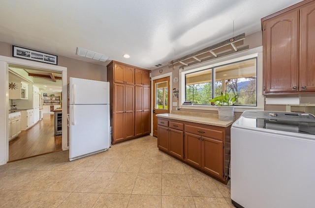kitchen with light countertops, visible vents, washer / dryer, light tile patterned floors, and freestanding refrigerator