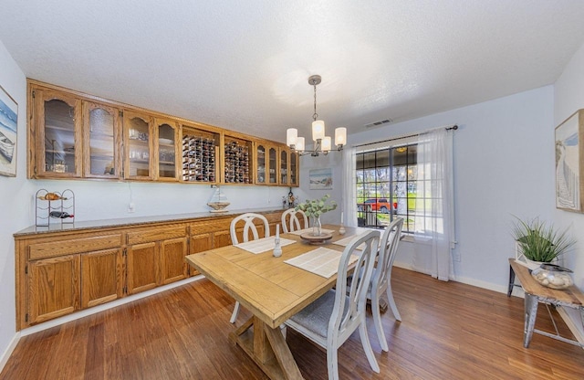 dining area with a chandelier, a textured ceiling, baseboards, visible vents, and dark wood-style flooring