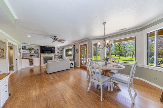 dining space with a textured ceiling, visible vents, crown molding, light wood-style floors, and a glass covered fireplace