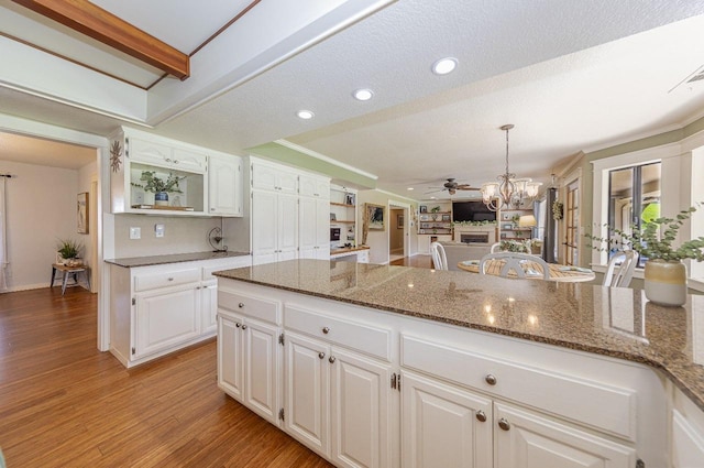 kitchen with pendant lighting, light wood-type flooring, ceiling fan with notable chandelier, white cabinets, and dark stone counters