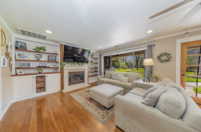 living area with crown molding, light wood finished floors, a glass covered fireplace, a textured ceiling, and visible vents