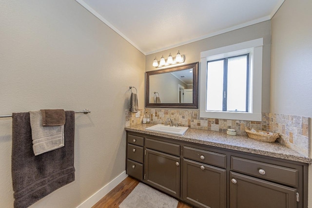bathroom featuring vanity, backsplash, wood finished floors, baseboards, and ornamental molding