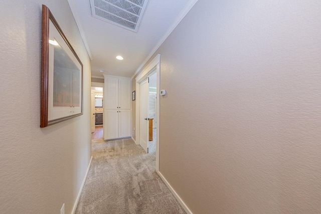 hall featuring baseboards, light colored carpet, visible vents, ornamental molding, and a textured wall