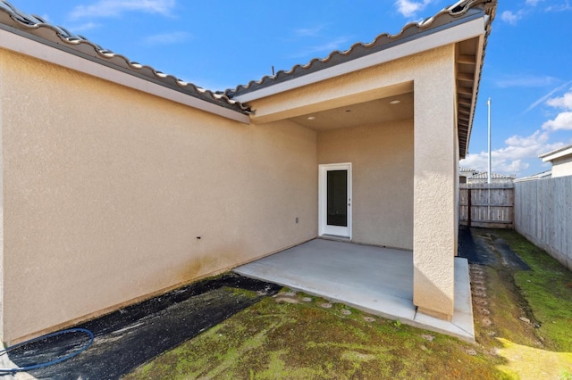 view of exterior entry featuring a patio area, a tile roof, fence, and stucco siding