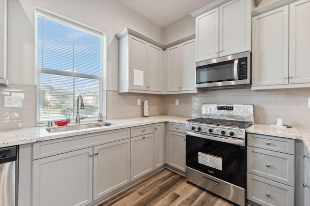 kitchen with backsplash, light stone countertops, stainless steel appliances, a sink, and wood finished floors