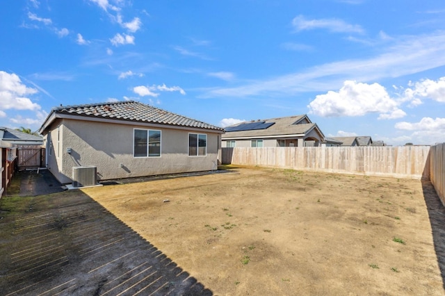 rear view of property featuring central air condition unit, a tiled roof, a fenced backyard, and stucco siding
