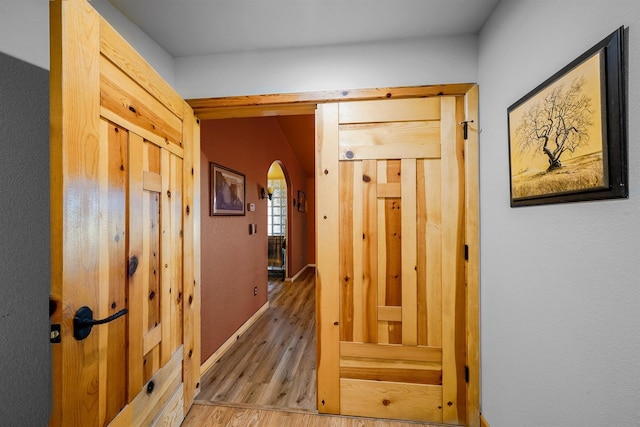 hallway featuring arched walkways and wood finished floors