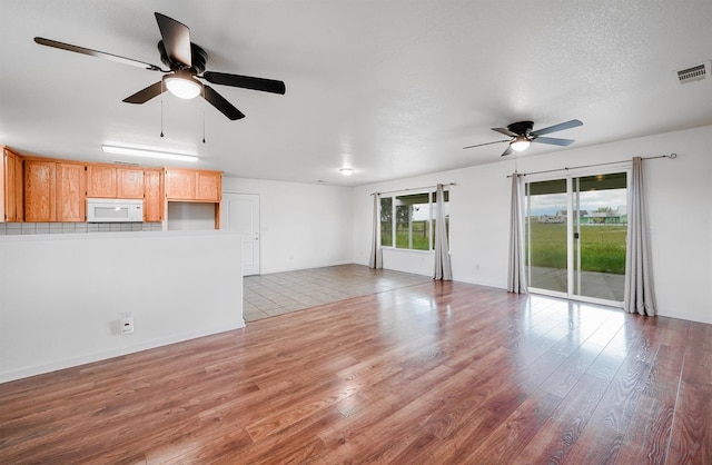 unfurnished living room featuring visible vents, a textured ceiling, light wood-style floors, and ceiling fan