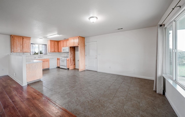 kitchen featuring light countertops, backsplash, baseboards, white appliances, and visible vents