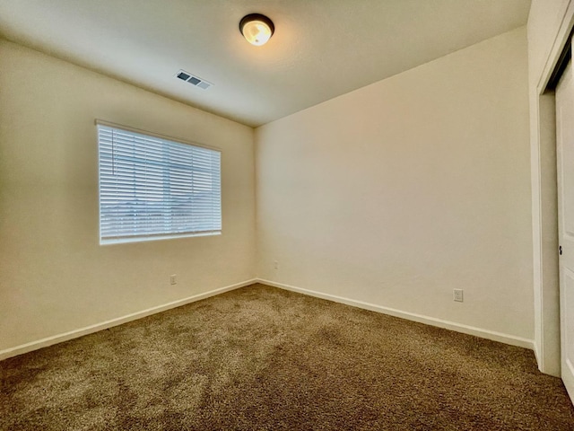 spare room featuring baseboards, visible vents, and dark carpet